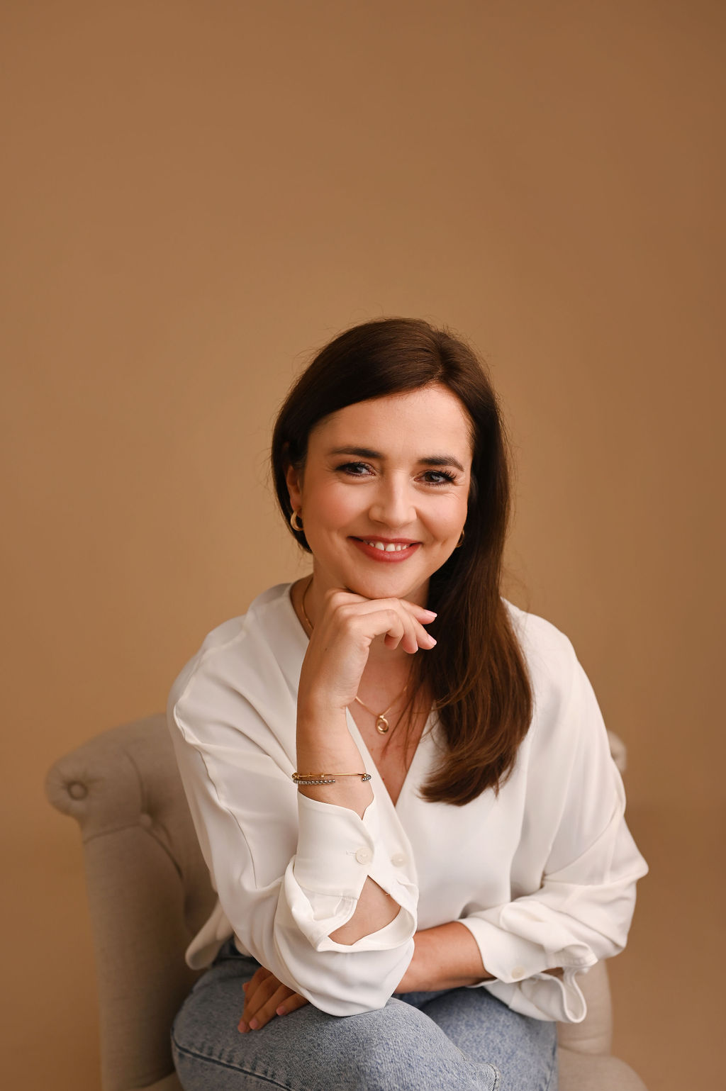 Joana Maciel sentada, de camisa branca, a sorrir para a câmara.